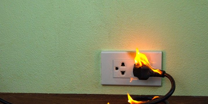 Electrical outlet with flames and burning cord, illustrating the dangers of electrical fires and the risks associated with faulty wiring.