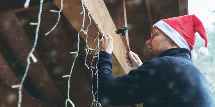 Person in a Santa hat hanging Christmas lights on a wooden structure, illustrating winter electrical safety and holiday decoration.