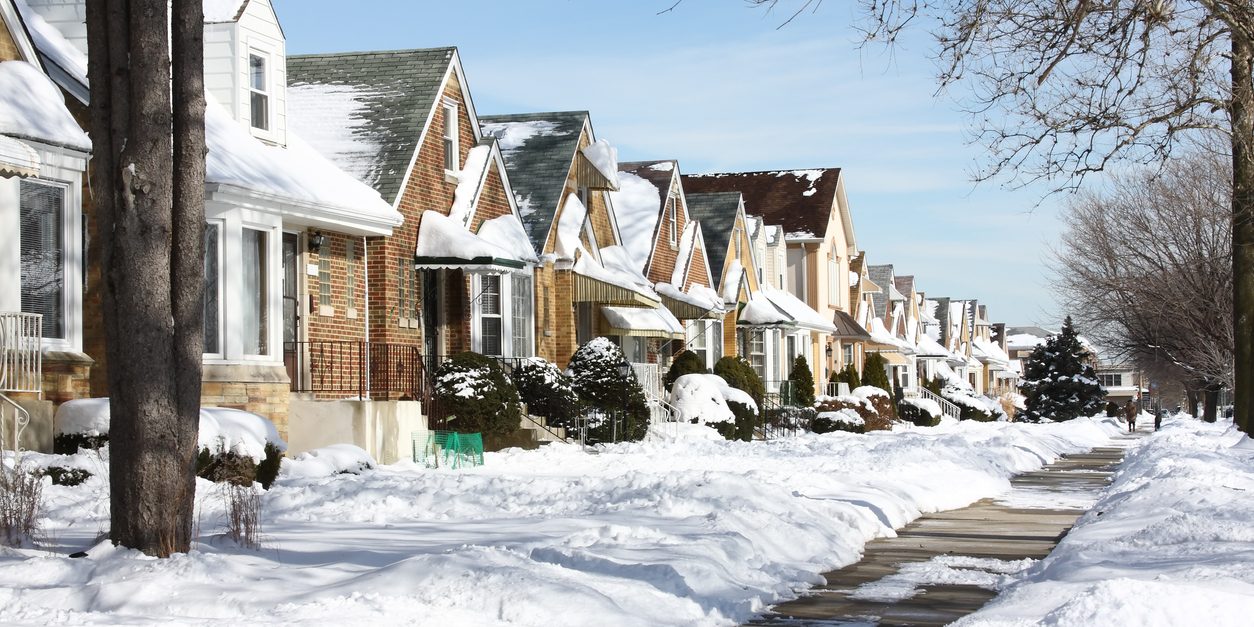 Snow-covered residential street with houses, showcasing winter scenery, emphasizing the need for winterization tips to save on electric bills.