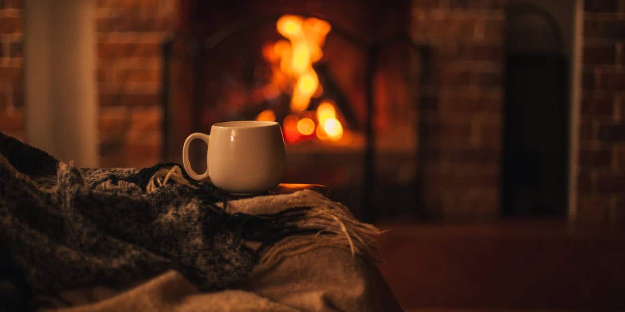 Mug with hot tea standing on a chair with woolen blanket in a cozy living room with fireplace. heater safety in warm home.